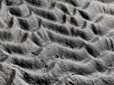 Monochrome close-up of rippled wet sand on a beach showing shadows, granules and small debris