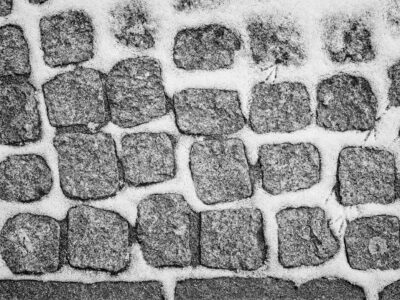 Black and white close-up of textured cobblestone pavement with snow-filled joints creating a high-contrast pattern