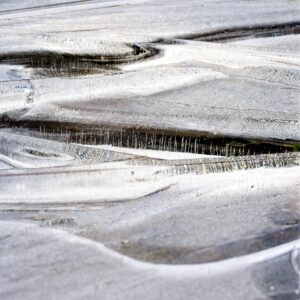 Close-up of frozen ice surface with rippled textures and vertical air bubble columns creating a monochrome abstract landscape