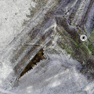 Close-up abstract texture photograph of cracked icy surface with frosty patterns, bubbles and dark crevices on frozen water