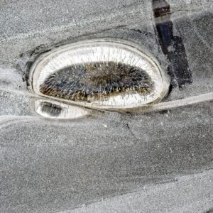 Aerial abstract of salt-encrusted evaporation ponds with white rims and spike-like salt crystals in muted grey tones
