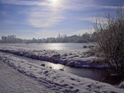 Sunlit frozen river with snow-covered banks and frosted trees in a serene Bernd Meyer winter landscape photo