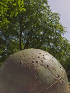 Close-up of bronze globe sculpture with embossed map detail in Rhododendron Park against green trees and sky
