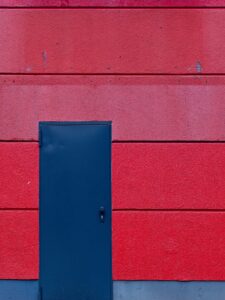 Close-up of a textured red facade with horizontal panel lines and a narrow matte navy service door on left