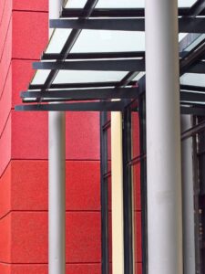 Close-up of modern storefront entrance with glass canopy, black steel beams and bold red textured exterior wall