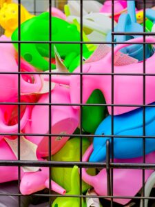 Close-up of colourful pink, green and blue plastic watering cans behind a black metal grid at a retail display