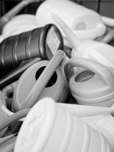 Black and white close-up of stacked plastic watering cans with curved handles and slim spouts