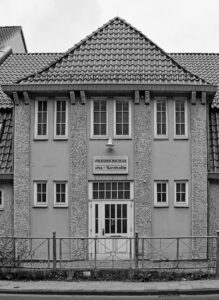 Black-and-white facade of Volkshochschule vhs-Turnhalle in Delmenhorst with tiled gable roof and symmetrical windows
