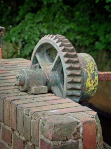 Weathered iron gear mechanism with moss and lichen resting on old red brick wall, close-up outdoor detail shot