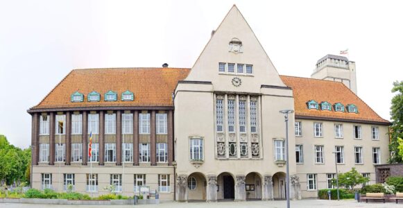 Panoramic shot of Delmenhorst town hall with ornate central gable, clock, arched entrance and red tiled roof in daylight