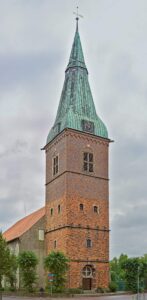 Tall red-brick church tower with green copper spire and clock against an overcast sky in Delmenhorst