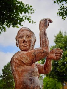 Bronze statue of a woman at Delmenhorst station raising an arm in tribute to wool‑mill workers, framed by trees and sky