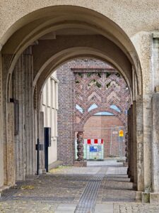 Stone arcade in Delmenhorst with layered concrete arches framing a decorative red-brick patterned archway and cobbled walkway